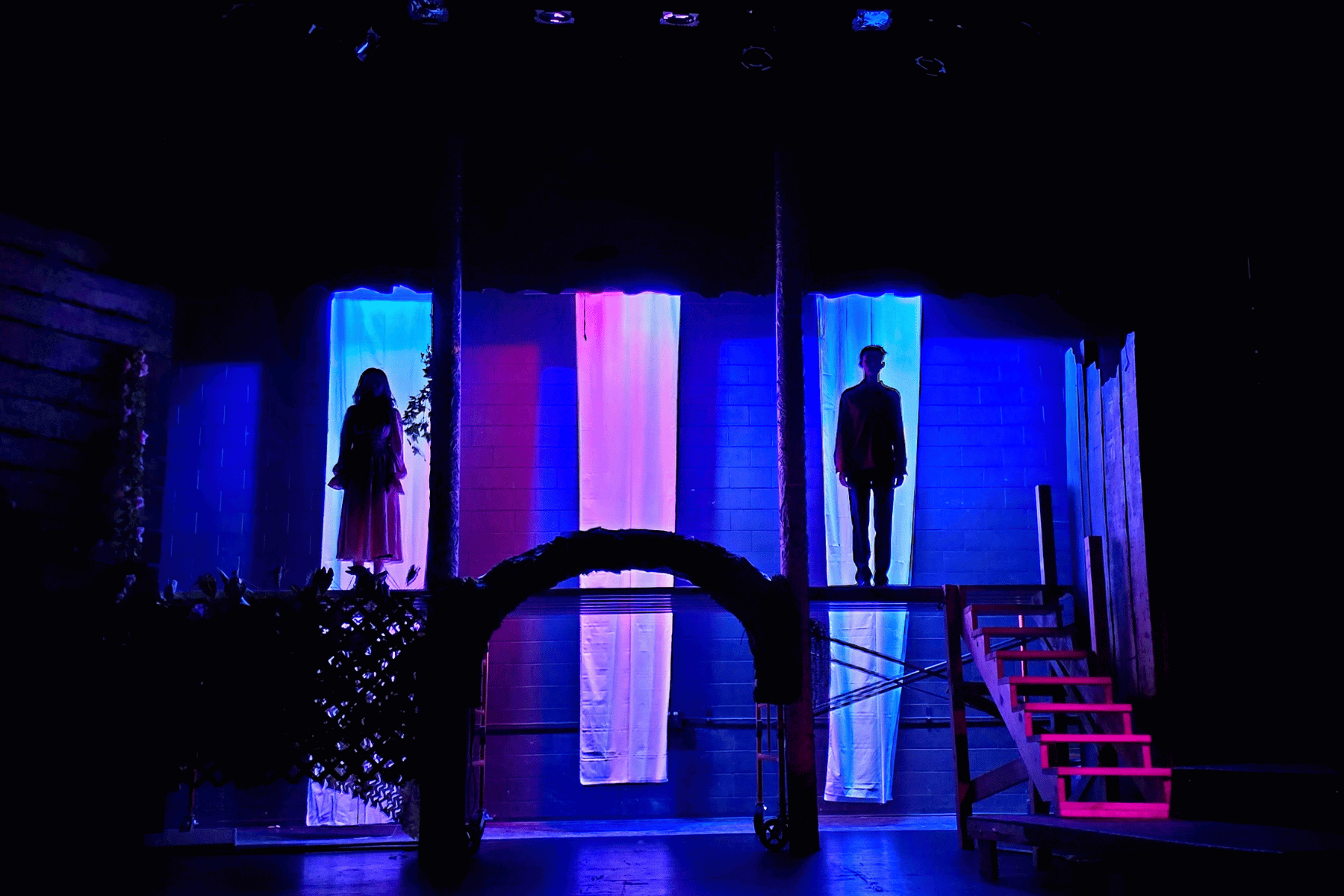 Purple and blue lights light a stage where Lake County High School students Karen Saucedo and Merritt Baker are silhouetted in the prologue of Romeo y Julieta.