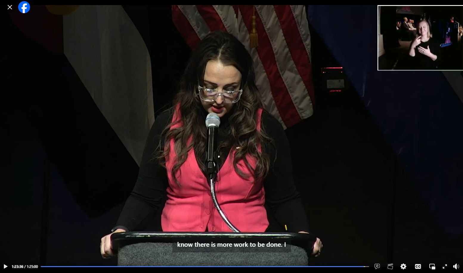 a person at a microphone on a podium in front of a U.S. Flag