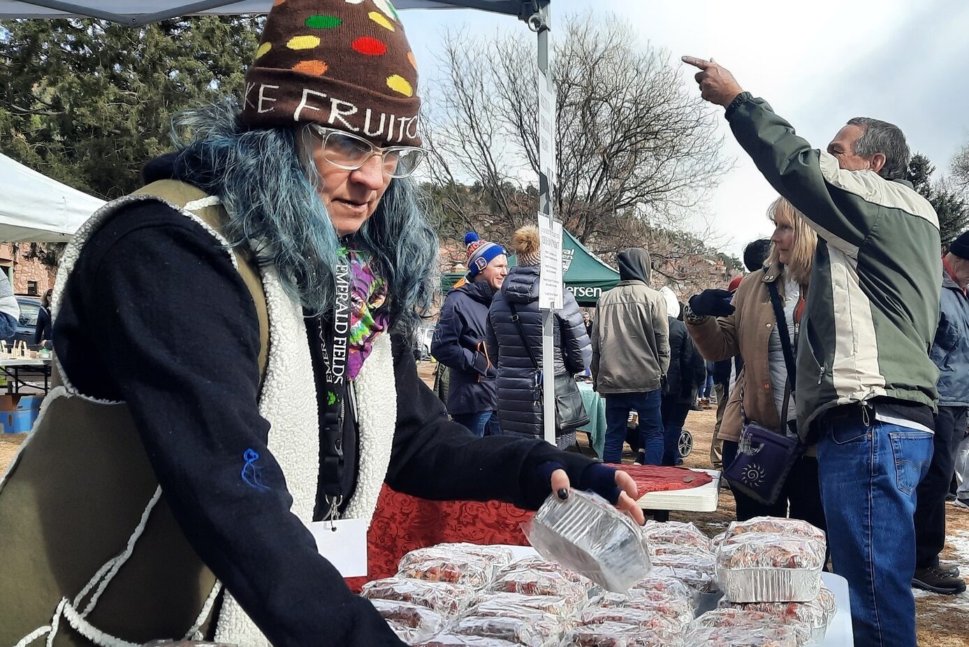 A woman wearing a fruitcake beanie arranges fruitcakes on a table.