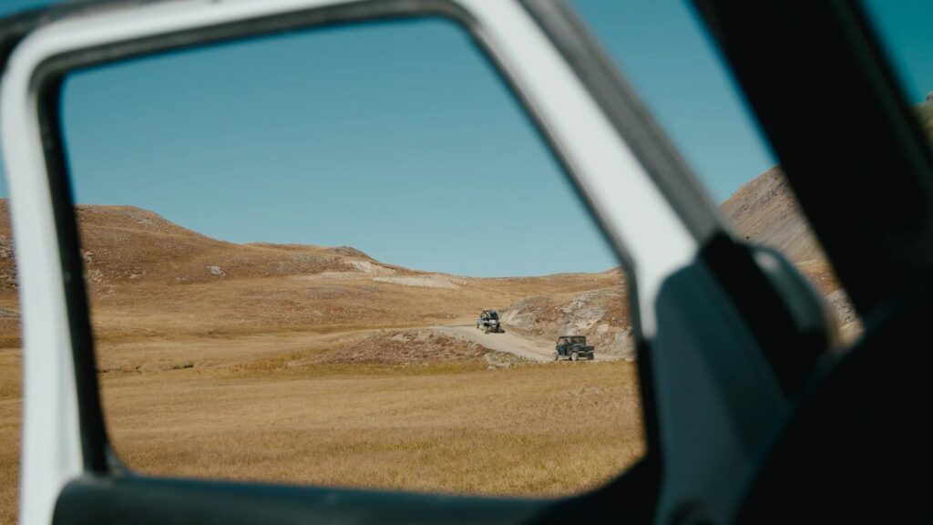 Two ATVs drive along a dirt road in the distance seen through an open car window