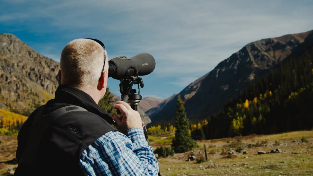 Terry Meyers uses binoculars to look at a mountain side in the distance