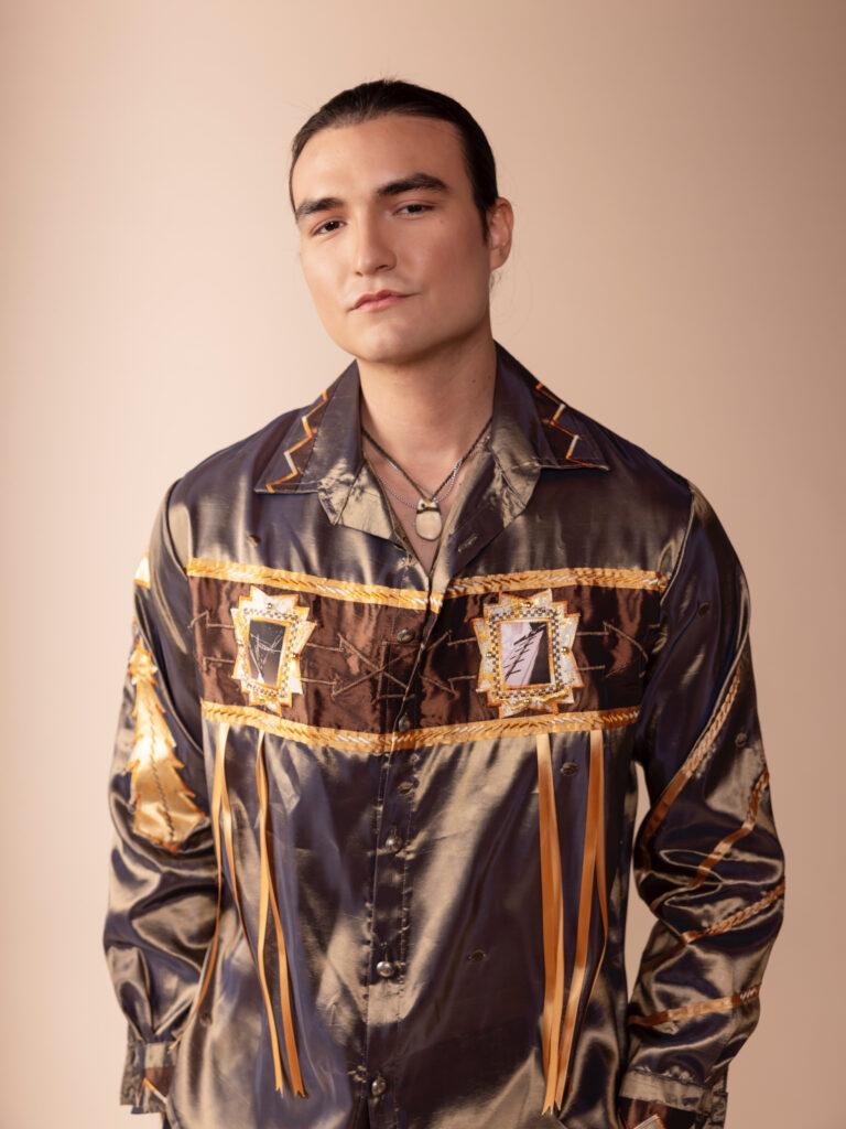 young native american man modeling a brown shiny shirt with applique designs with serious facial expression