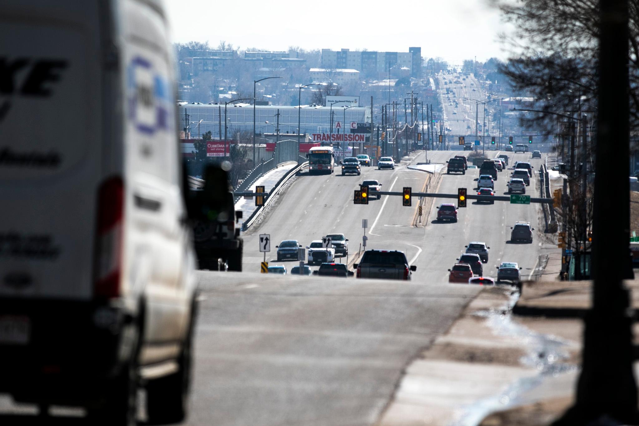 Cars on a long stretch of road pass on a street with houses and businesses in haze in the background.