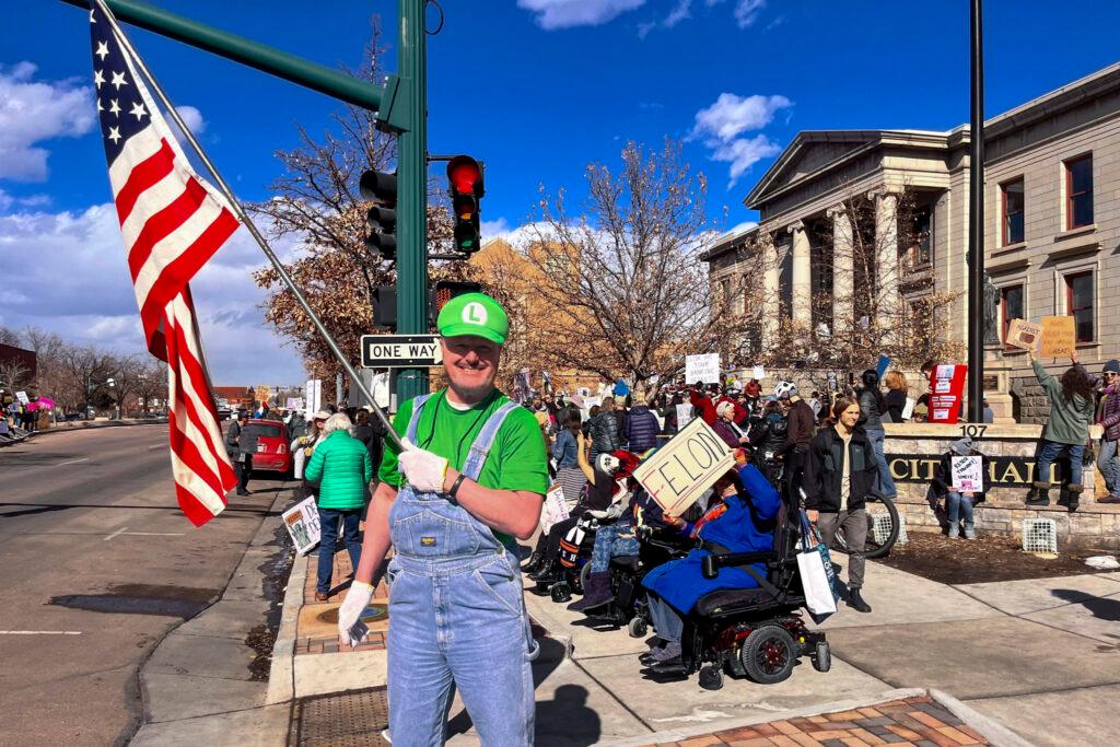 Man in costume waves flag with group of people behind him.