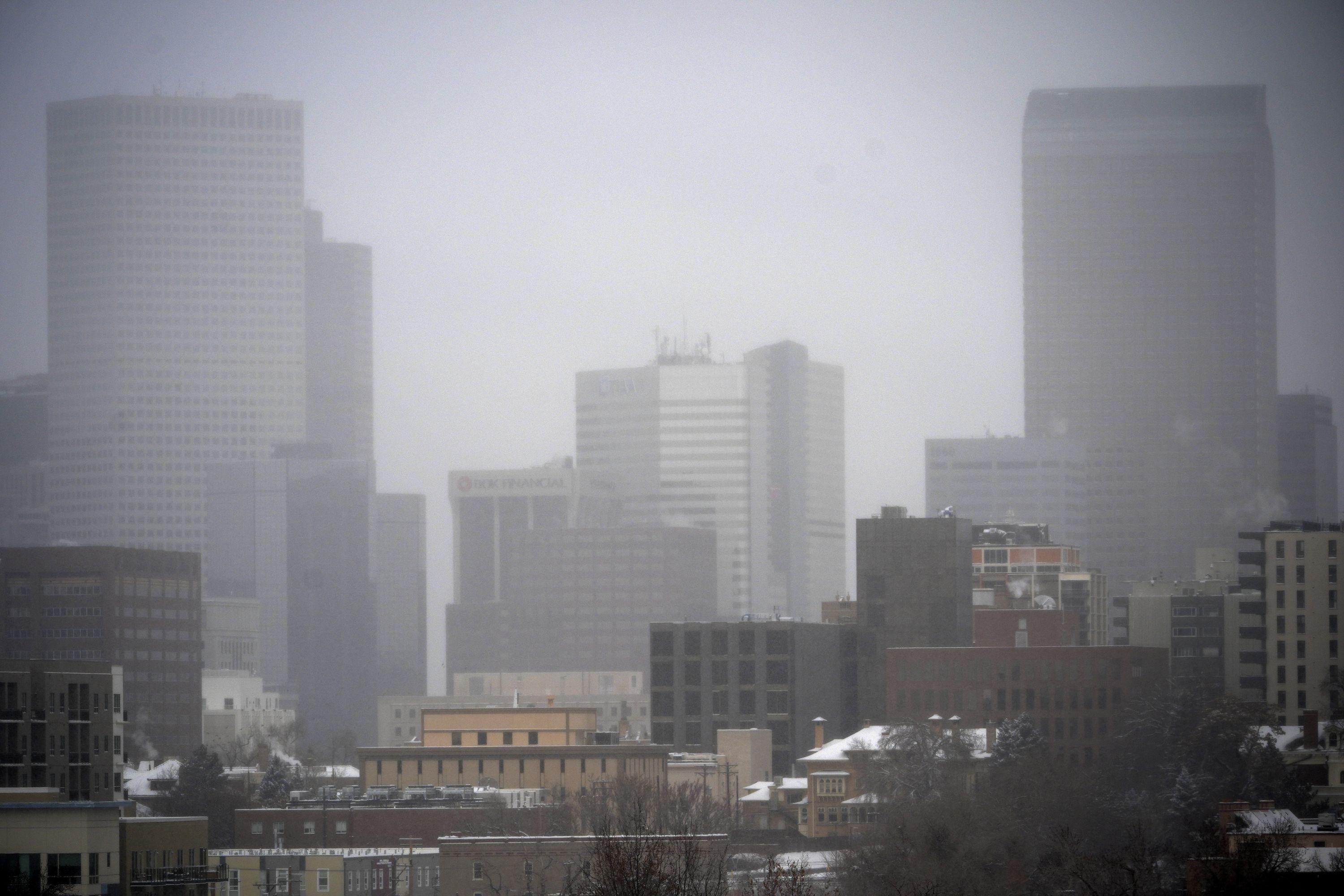 Downtown Denver shrouded in snowy mist with other buildings in the foreground.