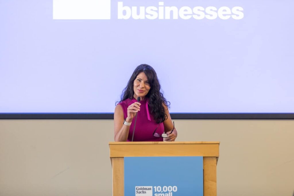 A woman in a pink dress speaks into a microphone at a lecturn.