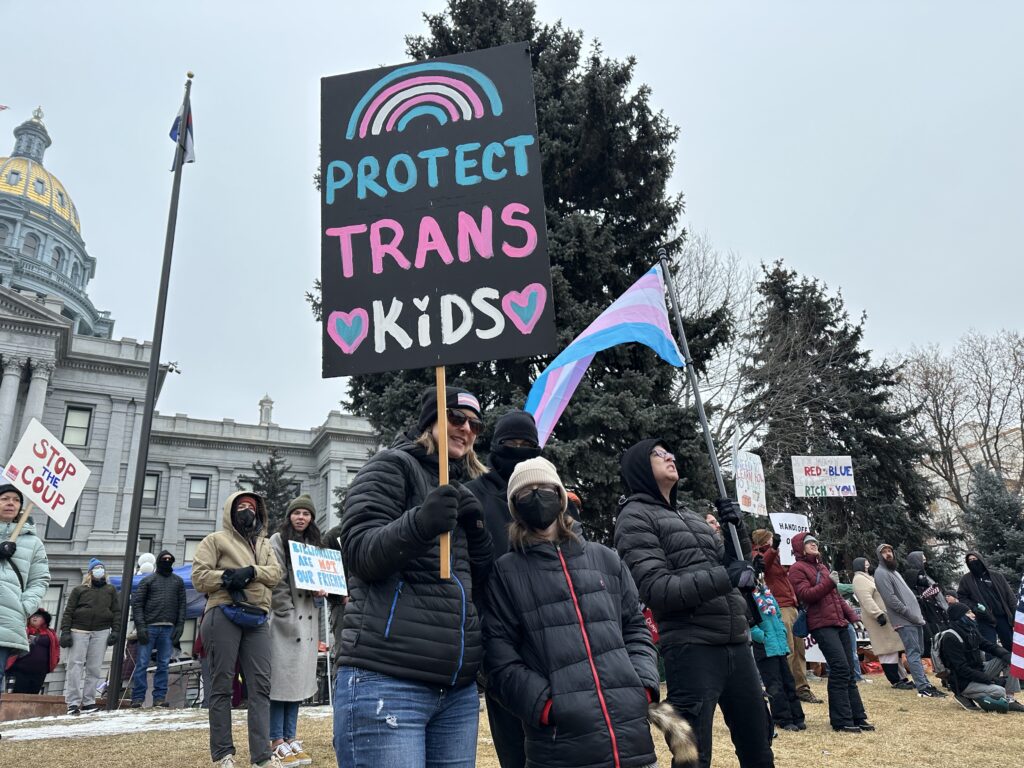 Protesters with a sign that says PROTECT TRANS KIDS stand outside the Colorado State Capitol.