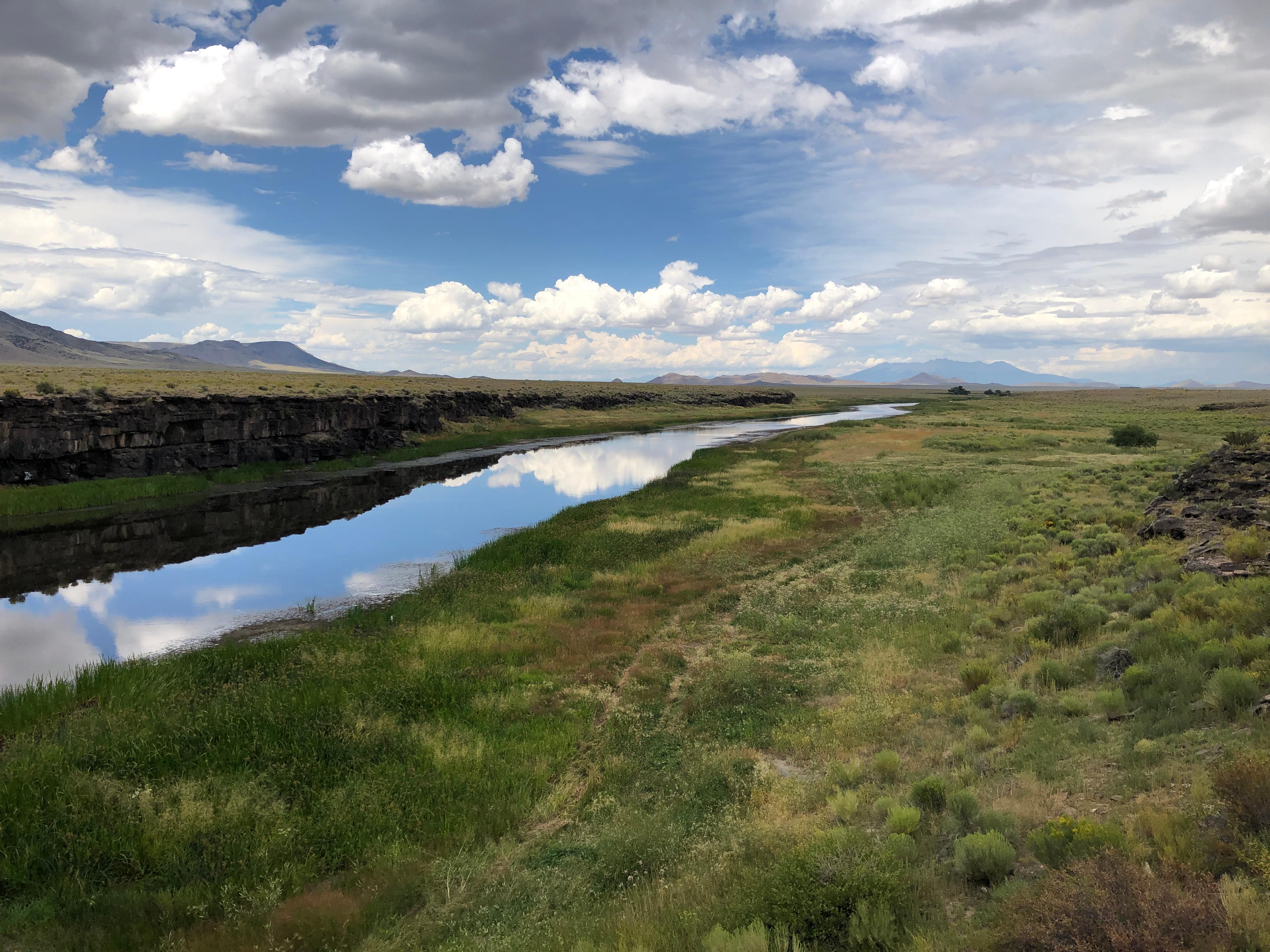 A river flows through an open landscape with mountains in the distance