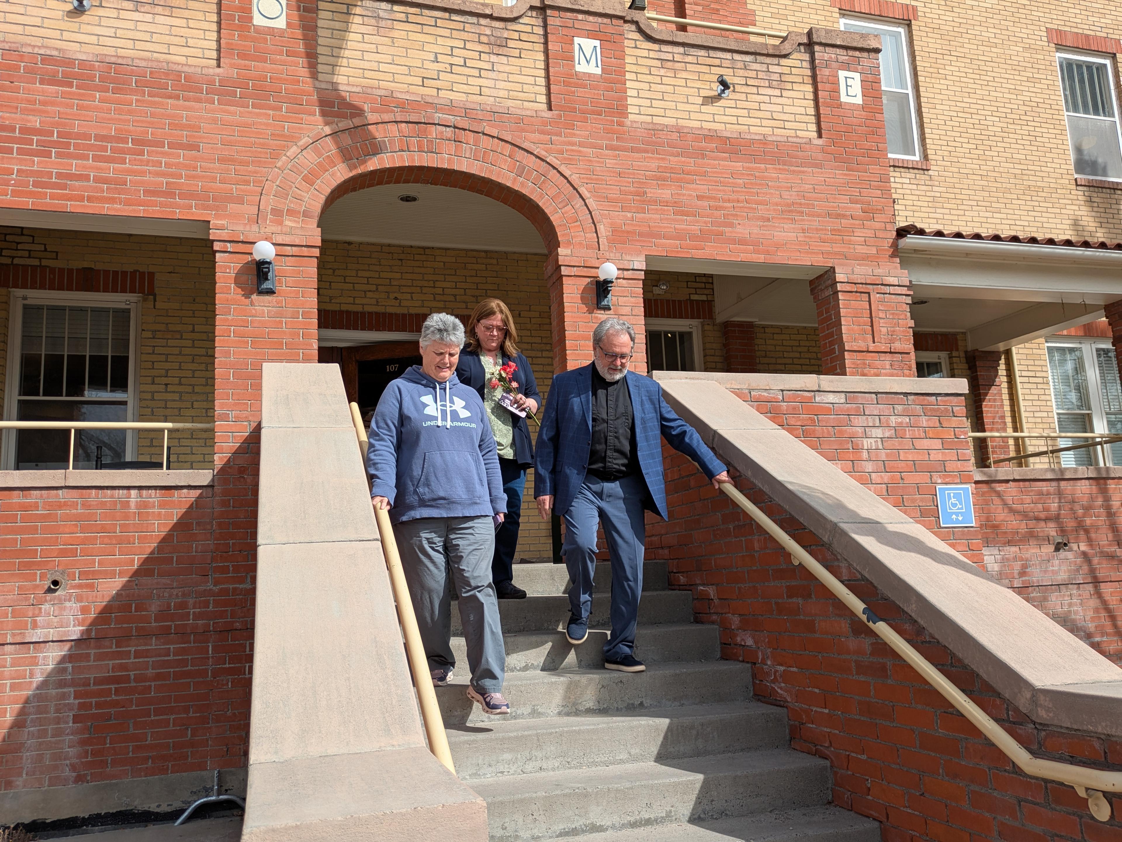 Reverend Kevin Young walks down a set of stairs that lead to the Elks Civic Building in Montrose. Young is wearing a blue, plaid sport coat over a black shirt with a clergy collar.