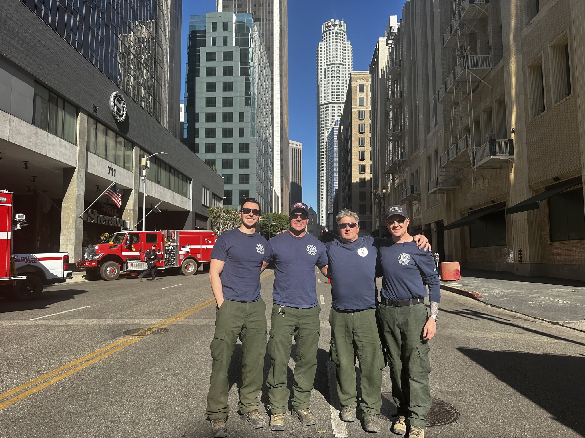 Four Colorado firefighters stand arm-in-arm on a street in downtown Los Angeles.