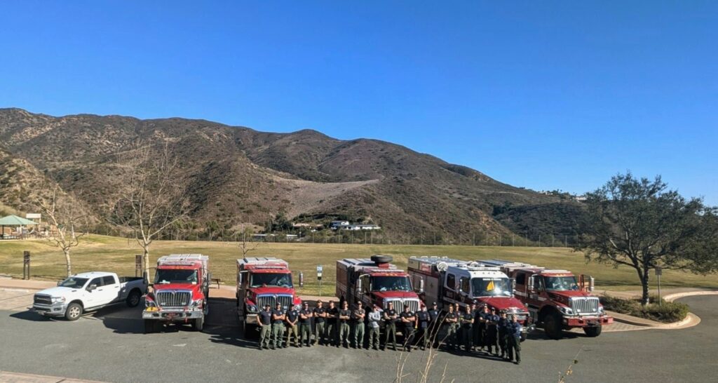 Colorado firefighting strike team gathers at a parking lot alongside five fire engines.