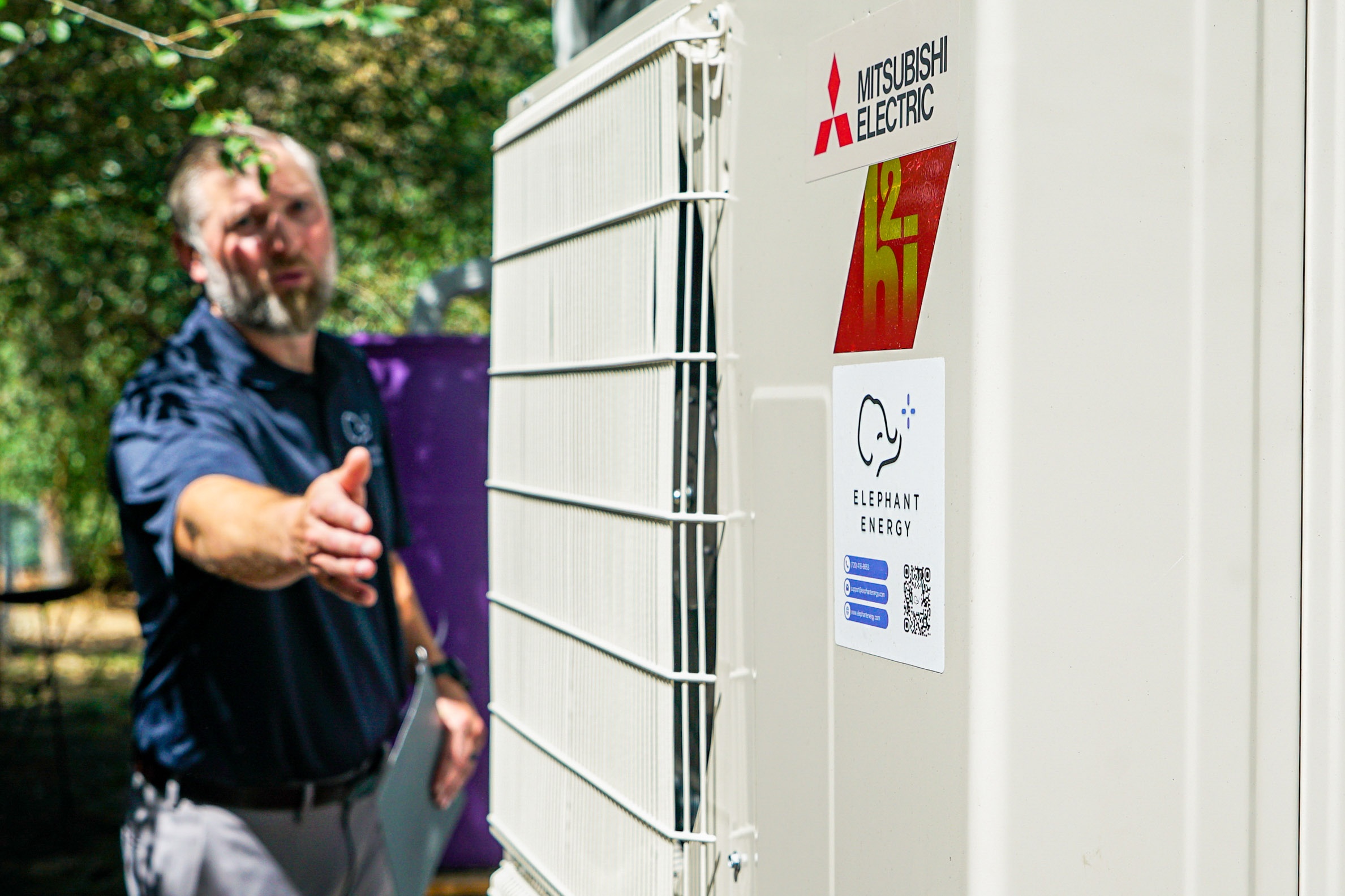 A worker in a blue shirt points at a heat pump installed outside a Denver home.