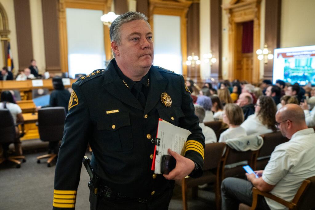 Teller County Sheriff Jason Mikesell, in dress blues, walks down the aisle of a packed hearing room at the state Capitol.