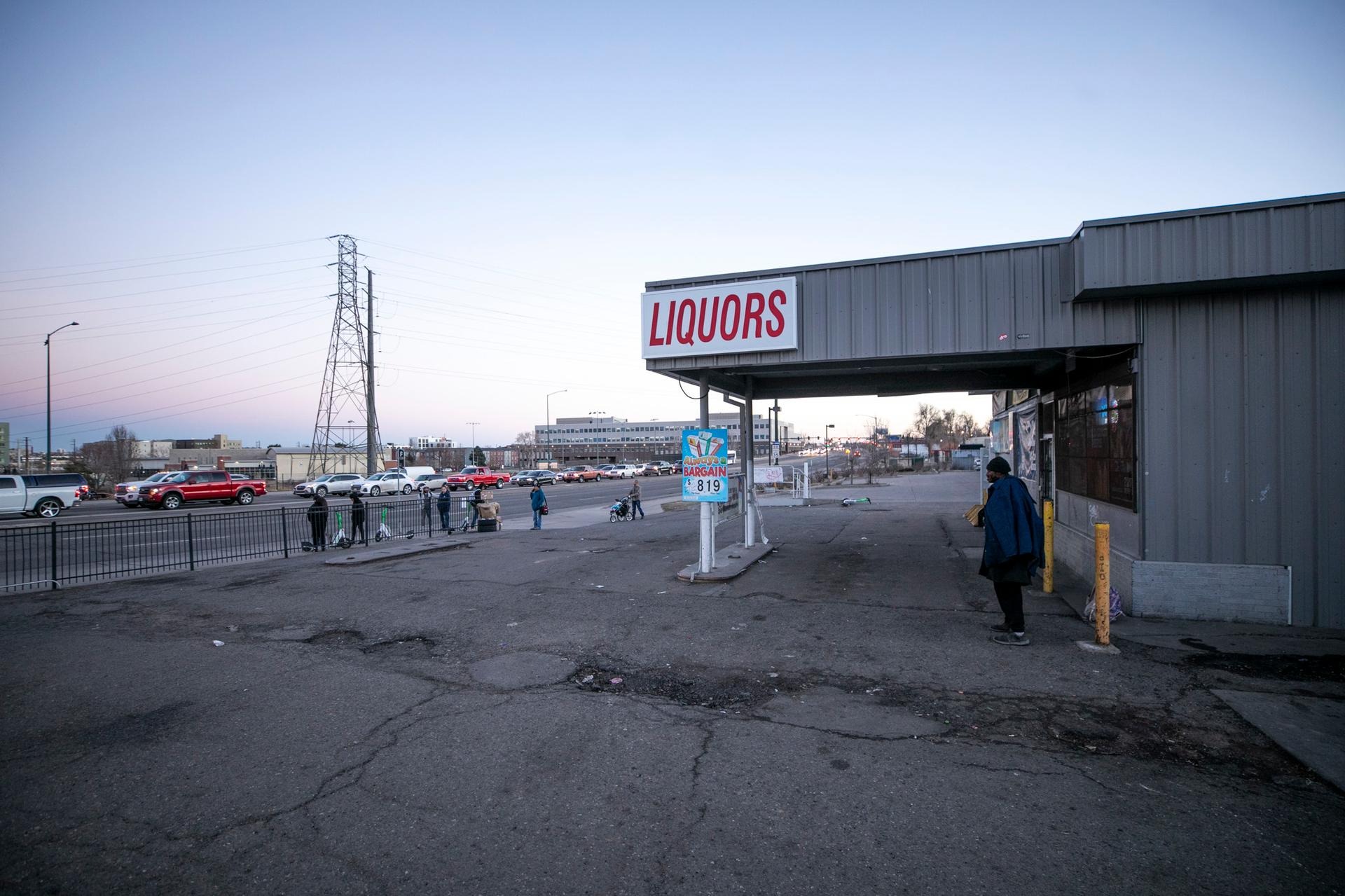 A man stands on cracked asphalt in front of the dilapidated-looking Avondale Liquors building.