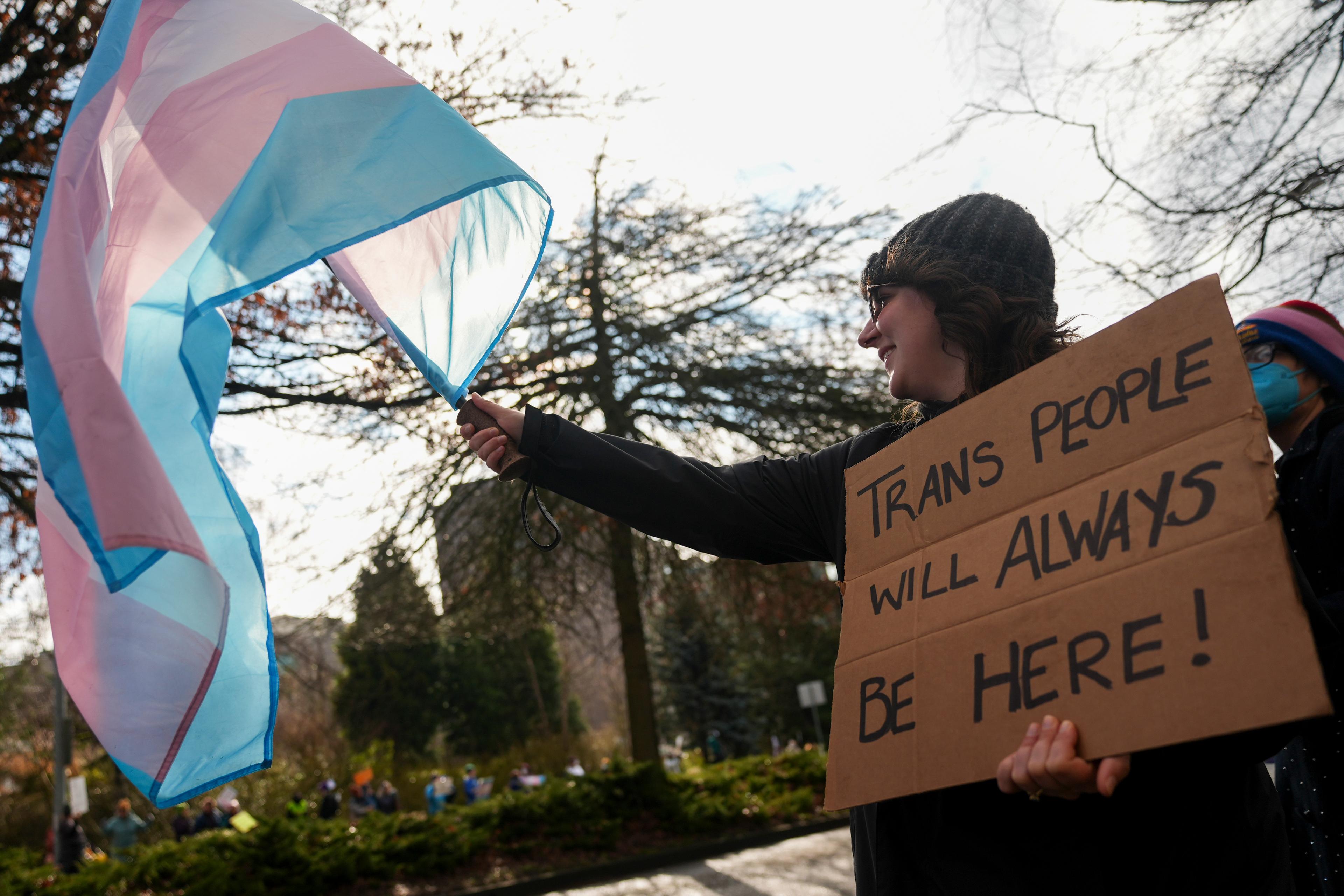 Protestor holds Trans flag and sign