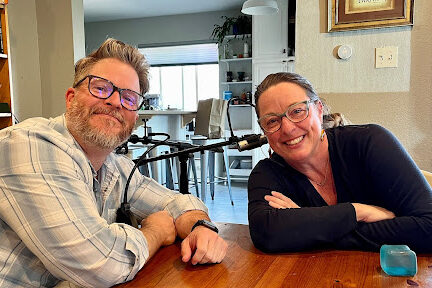 Podcast host Cody Hufstedler is shown smiling and leaning to the right while seated at a table with Aimee Dokes of Denver, who is also smiling. She is leaning inward from the right side of the photo.