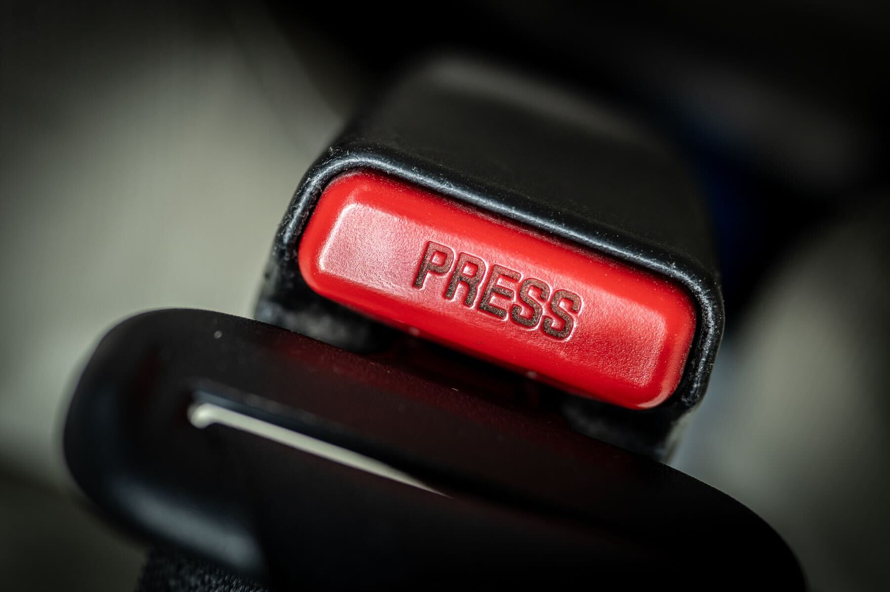 Close-up of a bright red "PRESS" button on a motor vehicle seat belt