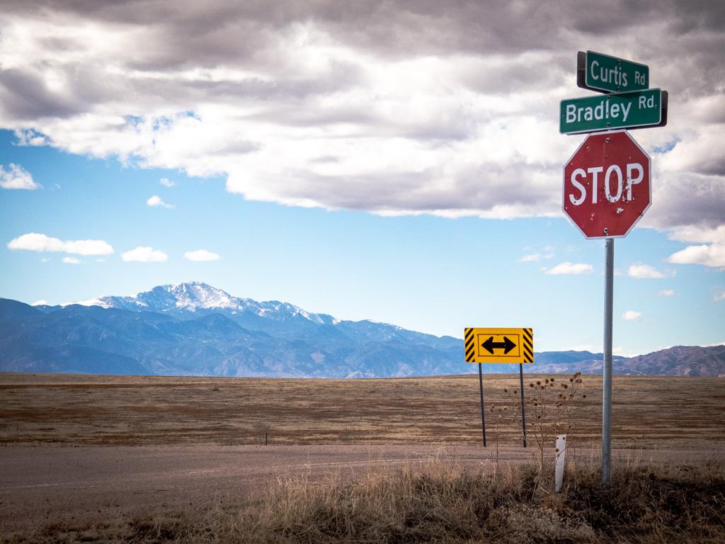 road, stop and other signs in a large open area with mountains in the background