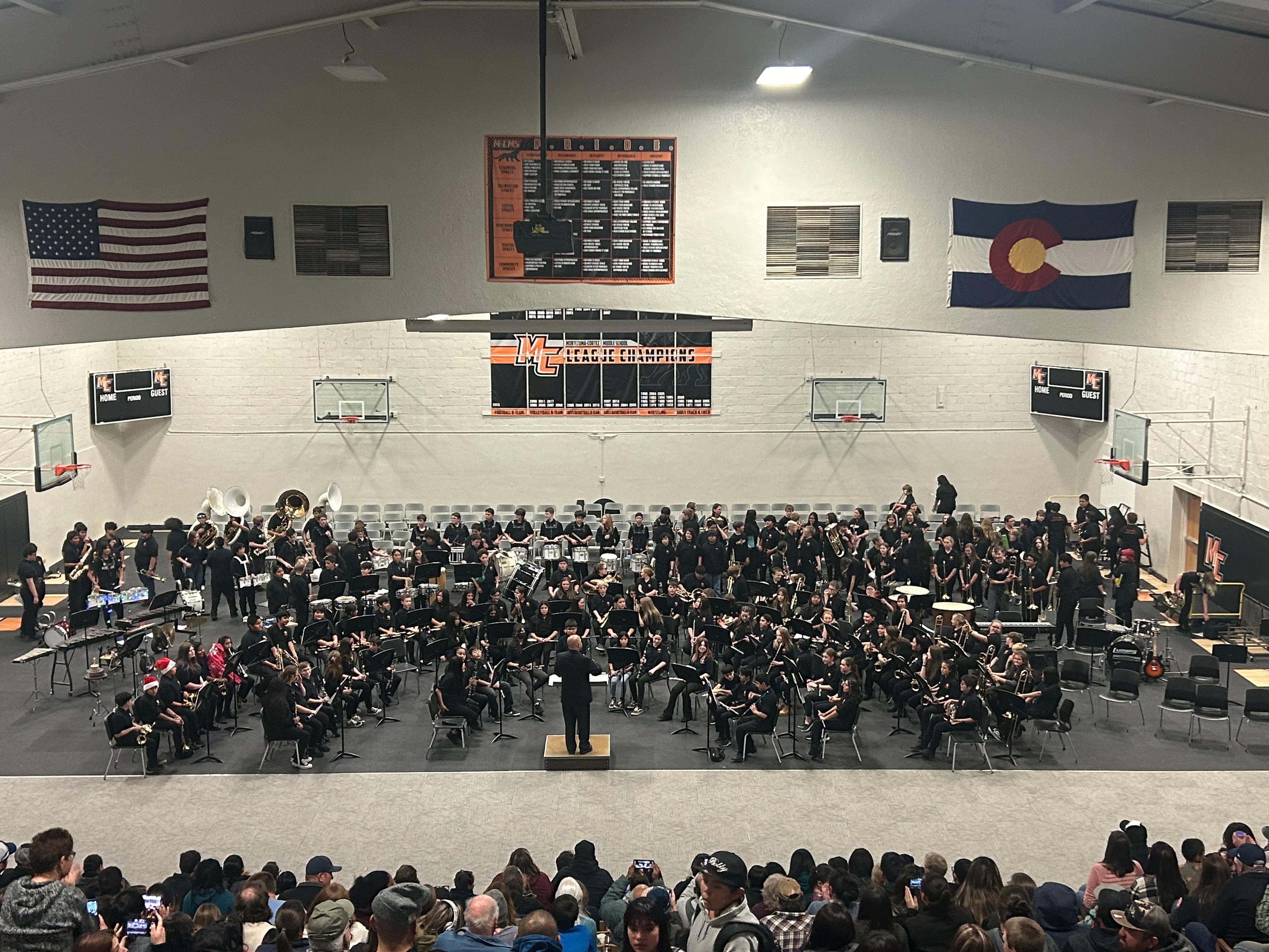 Conductor Andrew Campo stands on a podium in front of a large middle school band giving a concert in the Montezuma Cortez middle school gym.