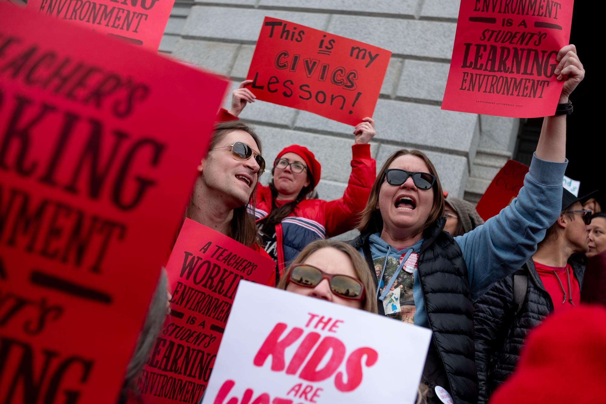 A picture of a crowd holding red signs that say "A teacher's working environment is a student's learning environment."