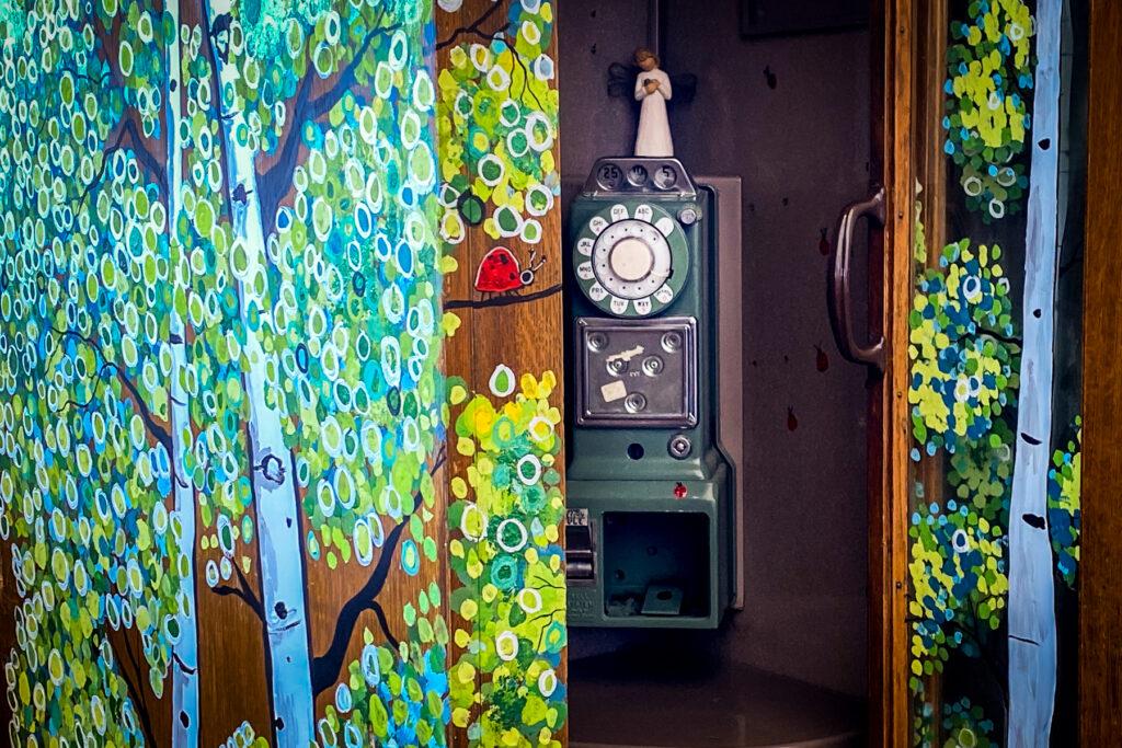 A wooden angel sits atop an old payphone that has been converted into a wind phone.