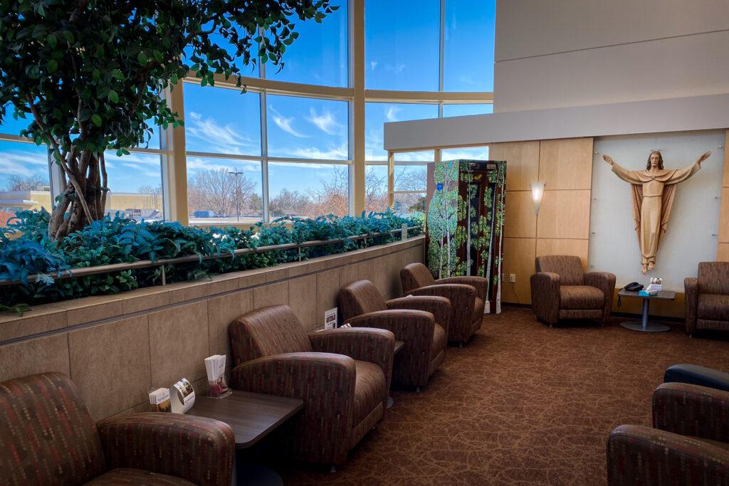 A phone booth decorated with trees sits in a sunny hospital waiting room.