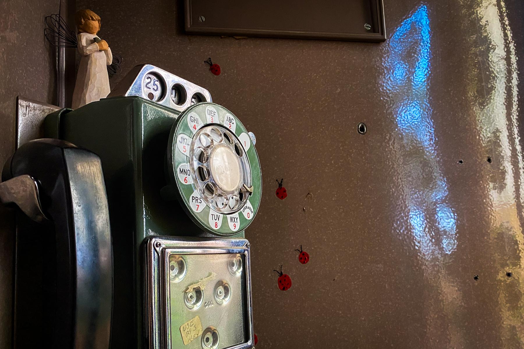 A wooden angel sits atop an old payphone that has been converted into a wind phone.